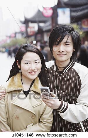 Portrait of a young man holding a mobile phone with a young woman smiling View Large Photo Image Stock Photograph - Portrait of a young man holding a mobile phone with a young woman smiling. Fotosearch