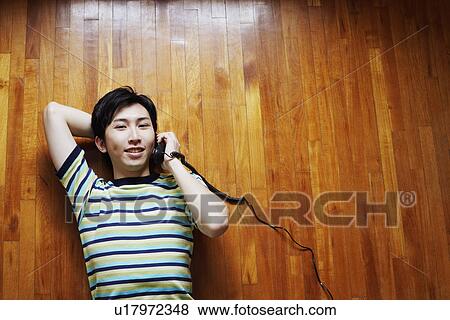 Portrait of a young man talking on the telephone and lying on a hardwood floor View Large Photo Image Stock Photo - Portrait of a young man talking on the telephone and lying on a hardwood floor. Fotosearch