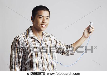 Portrait of a young man wearing headphones and holding a mobile phone View Large Photo Image Stock Photo - Portrait of a young man wearing headphones and holding a mobile phone. Fotosearch