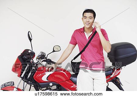 Young man talking on a mobile phone and leaning against a motorcycle View Large Photo Image Stock Photography - Young man talking on a mobile phone and leaning against a motorcycle. Fotosearch