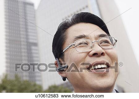 Stock Image - Low angle view of a businessman wearing a hands free device smiling. Fotosearch