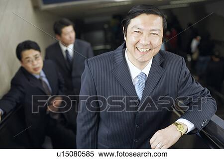 Stock Photography - Portrait of a businessman standing on an escalator smiling. Fotosearch