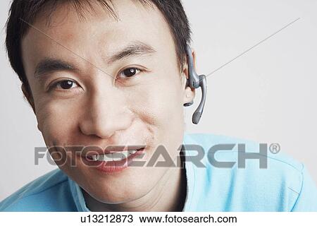 Stock Image - Portrait of a young man wearing a hands-free device and smiling. Fotosearch