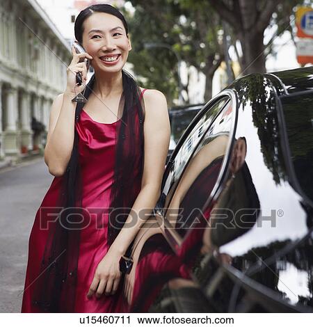 Stock Image - Businesswoman leaning against a car and talking on a mobile phone. Fotosearch