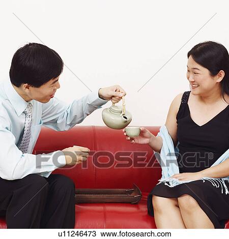 Stock Image - Close-up of a businessman pouring tea in a tea cup held by a mid adult woman. Fotosearch