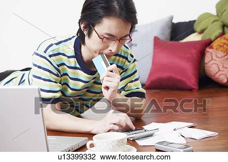 Stock Image - Mid adult man calculating bills using a calculator. Fotosearch