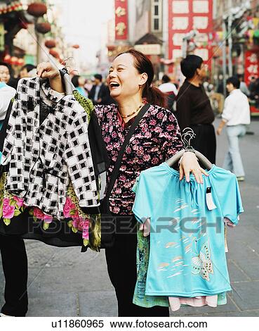 Stock Photography - Mid adult woman holding garments and laughing. Fotosearch