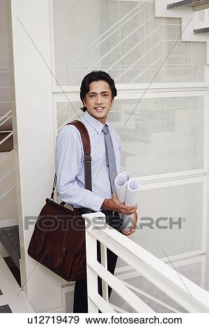 Portrait of a male architect holding rolled up blueprints and smiling View Large Photo Image Stock Photo - Portrait of a male architect holding rolled up blueprints and smiling. Fotosearch