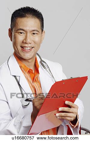 Portrait of a male doctor writing on a clipboard and smiling View Large Photo Image Stock Photo - Portrait of a male doctor writing on a clipboard and smiling. Fotosearch