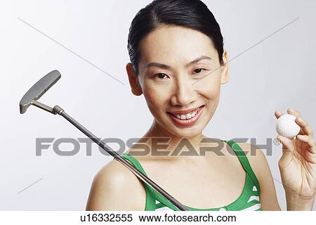 Stock Photography - Portrait of a mid adult woman holding a golf club and a golf ball. Fotosearch