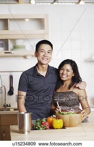 Stock Photo - Portrait of a young man standing with a mid adult woman in the kitchen. Fotosearch