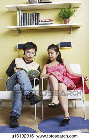 Stock Photograph - Young man and a mid adult woman sitting on chairs listening to music. Fotosearch