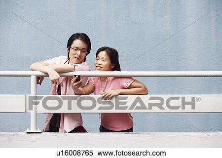 Young woman and a mid adult man looking at a mobile phone View Large Photo Image Stock Photography - Young woman and a mid adult man looking at a mobile phone. Fotosearch