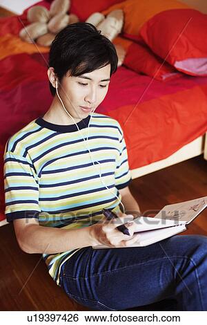 Stock Photograph - Close-up of a young man listening to music and reading a diary. Fotosearch