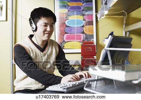 Close-up of a young man using a computer listening to music on headphones View Large Photo Image Stock Photo - Close-up of a young man using a computer listening to music on headphones. Fotosearch