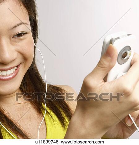 Close-up of a young woman holding a mobile phone and listening to music View Large Photo Image Stock Photograph - Close-up of a young woman holding a mobile phone and listening to music. Fotosearch
