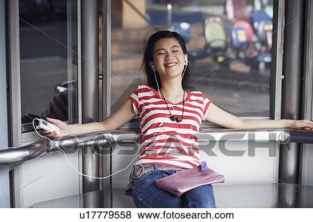 Close-up of a young woman listening to music and sitting in an elevator View Large Photo Image Stock Photo - Close-up of a young woman listening to music and sitting in an elevator. Fotosearch