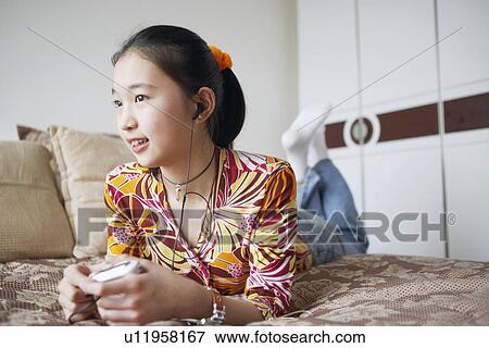 Close-up of a young woman lying on the bed listening to music View Large Photo Image Stock Photo - Close-up of a young woman lying on the bed listening to music. Fotosearch