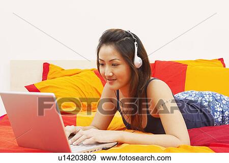 Close-up of a young woman using a laptop and listening to music on headphones View Large Photo Image Stock Photo - Close-up of a young woman using a laptop and listening to music on headphones. Fotosearch