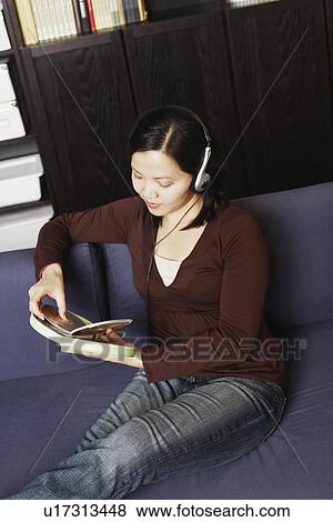Stock Photo - High angle view of a young woman holding a CD case listening to music with headphones. Fotosearch