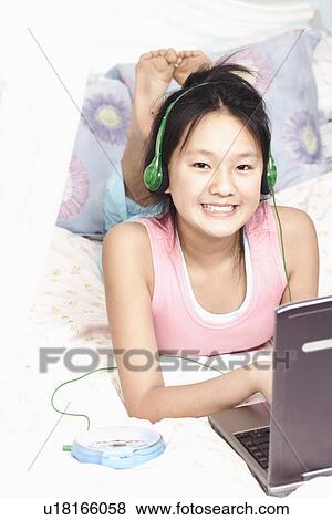 Stock Photo - Portrait of a girl using a laptop and listening to music on an MP3 player. Fotosearch