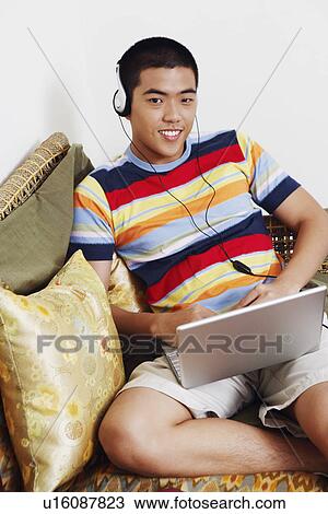 Portrait of a young man listening to music and using a laptop View Large Photo Image Stock Image - Portrait of a young man listening to music and using a laptop. Fotosearch
