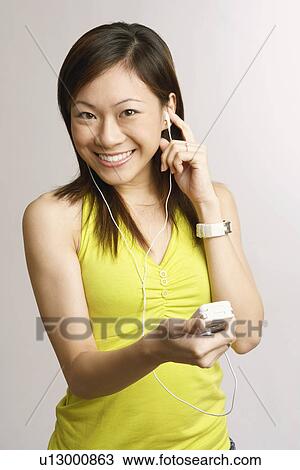 Portrait of a young woman holding a mobile phone and listening to music View Large Photo Image Stock Image - Portrait of a young woman holding a mobile phone and listening to music. Fotosearch