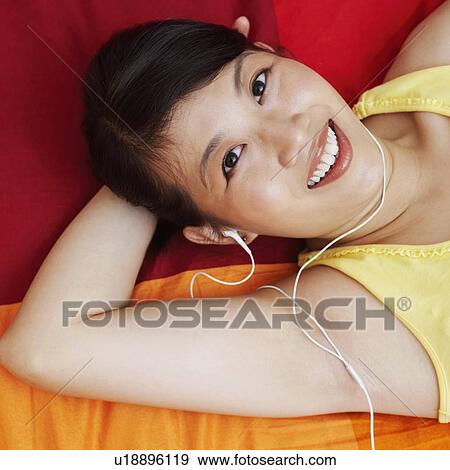 Portrait of a young woman listening to music and lying on the bed View Large Photo Image Stock Photo - Portrait of a young woman listening to music and lying on the bed. Fotosearch