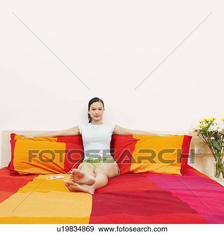Stock Photo - Portrait of a young woman reclining on the bed and listening to music on headphones. Fotosearch