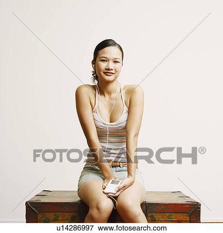 Stock Photo - Portrait of a young woman sitting on a trunk and listening to music. Fotosearch