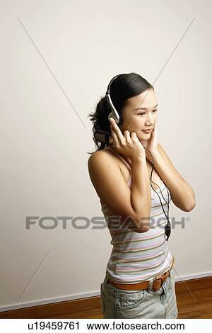 Stock Image - Side profile of a young woman listening to music and holding a mobile phone. Fotosearch