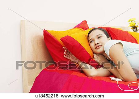 Side profile of a young woman lying on the bed and listening to music on headphones View Large Photo Image Stock Photograph - Side profile of a young woman lying on the bed and listening to music on headphones. Fotosearch