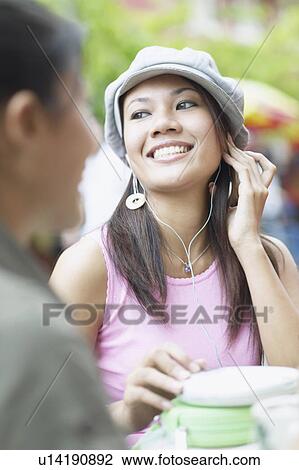 Stock Image - Young woman listening to music in an outdoor restaurant. Fotosearch