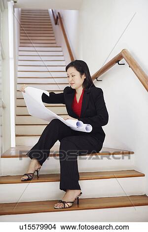 Picture - Businesswoman sitting on a staircase and looking at charts. Fotosearch
