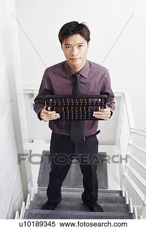 Stock Photography - High angle view of a businessman standing on a staircase and holding an abacus. Fotosearch