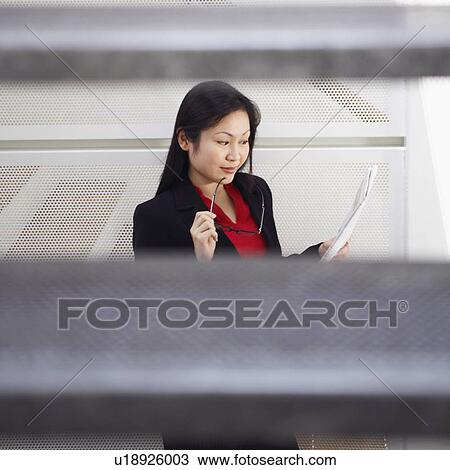 Stock Image - High angle view of a businesswoman holding eyeglasses and reading a newspaper. Fotosearch