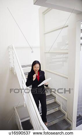 Stock Photo - High angle view of a businesswoman holding a newspaper and walking down a staircase. Fotosearch