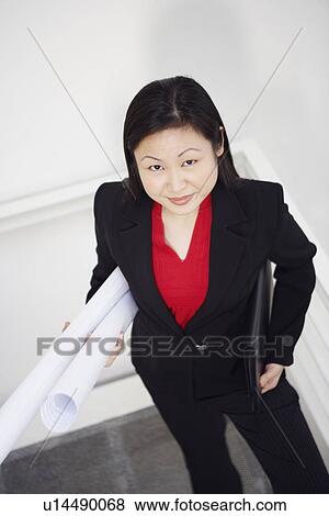 Stock Photo - Portrait of a businesswoman carrying rolled up charts and smiling. Fotosearch
