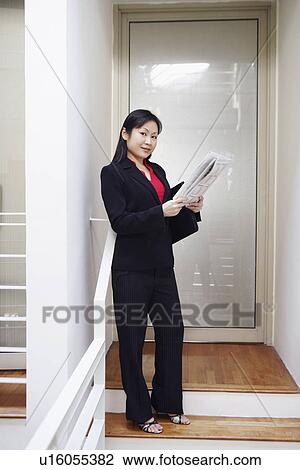 Stock Image - Portrait of a businesswoman holding a newspaper and smiling. Fotosearch