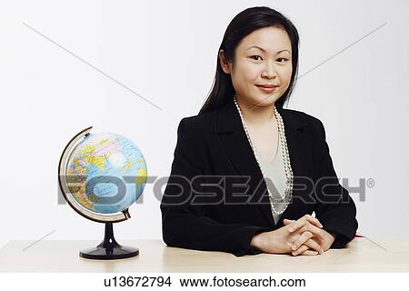 Picture - Portrait of a businesswoman sitting in an office with a globe in front of her. Fotosearch
