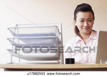 Stock Image - Portrait of a businesswoman sitting in an office and smiling. Fotosearch