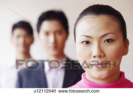 Stock Image - Portrait of a businesswoman with two businessmen in the background. Fotosearch