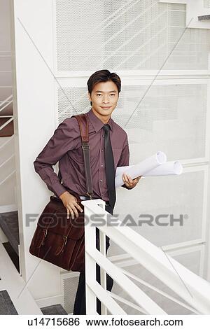 Stock Photograph - Portrait of a male architect holding rolled up blueprints and smiling. Fotosearch