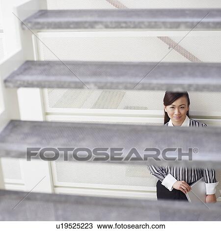 Stock Image - Portrait of a young woman leaning against a wall and holding a laptop. Fotosearch