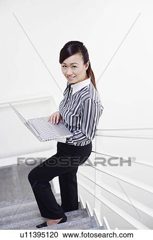 Portrait of a young woman standing on a staircase and using a laptop View Large Photo Image Stock Image - Portrait of a young woman standing on a staircase and using a laptop. Fotosearch