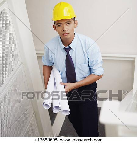 Stock Photography - Portrait of an architect walking down stairs and carrying blueprints. Fotosearch