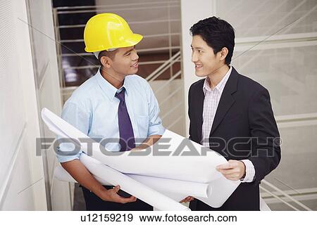 Stock Photo - Side profile of a businessman and an architect holding blueprints. Fotosearch
