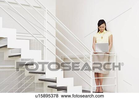Young woman leaning against a wall and using a laptop View Large Photo Image Stock Photo - Young woman leaning against a wall and using a laptop. Fotosearch