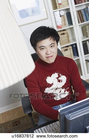 Stock Image - High angle view of a businessman sitting in front of a computer smiling. Fotosearch