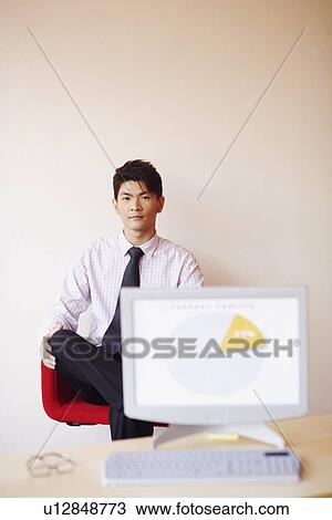 Stock Image - Portrait of a businessman sitting in an office in front of a model of a computer monitor. Fotosearch